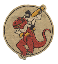 This is a patch for the 327th Bombardment Squadron, 92nd Bomb Group. The patch is worn on the left side of a flight jacket. The patch depicts a prehistoric cave man (Ollie OOP) ridding on a dinosaur (Denny) and charging into battle with a bomb in hand.