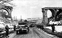 The 1st Battalion, 26th Infantry passing through the railway viaduct north of Bütgenbach, Belgium, on the Monschauer St. (N647) towards Bütgenbach. The railway viaduct was part of the line running from Losheim/Eifel (Germany) to Trois-Ponts, Belgium, and had been blown up by the retreating German troops.
