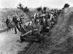 British army soldiers of the Royal Engineers engaged on mine clearing duties, pass a six pounder anti tank gun and carriers on a road near Lebisey Wood, one mile from the town of Caen during the Allied attack on the town.